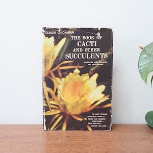 Op de afbeelding: Een vintage boek getiteld "The Book of Cacti and Other Succulents" van Claude Chidamian. De omslag toont een close-up van een gele en witte cactusbloem met groene bladeren.