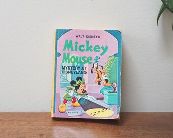 Op de afbeelding: Een vintage paperback boek getiteld "Walt Disney's Mickey Mouse Mystery at Disneyland" met een cartoonillustratie van Mickey Mouse en Pluto op de omslag.