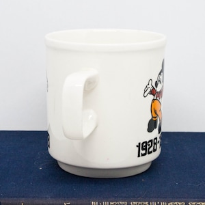 May include: White ceramic mug featuring a cartoon image of Mickey Mouse and the text "1928-1988 60 Years of Magic".