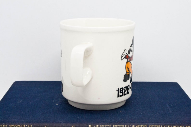 May include: White ceramic mug featuring a cartoon image of Mickey Mouse and the text "1928-1988 60 Years of Magic".