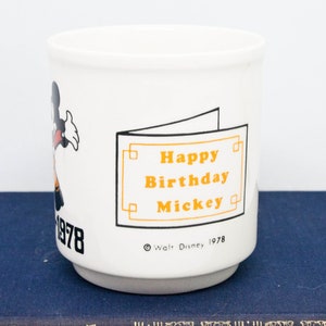 May include: White ceramic mug featuring a cartoon image of Mickey Mouse and the text "Happy Birthday Mickey" in orange. The mug also has the text "Walt Disney 1978" and "1978" on the side.