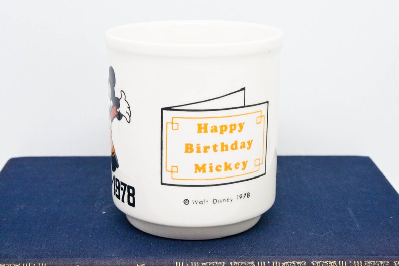 May include: White ceramic mug featuring a cartoon image of Mickey Mouse and the text "Happy Birthday Mickey" in orange. The mug also has the text "Walt Disney 1978" and "1978" on the side.