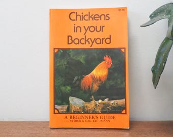 May include: An orange book titled "Chickens in Your Backyard: A Beginner's Guide by Rick & Gail Luttmann" with a price of $3.95. The cover features a close-up of a rooster in a green grassy area.