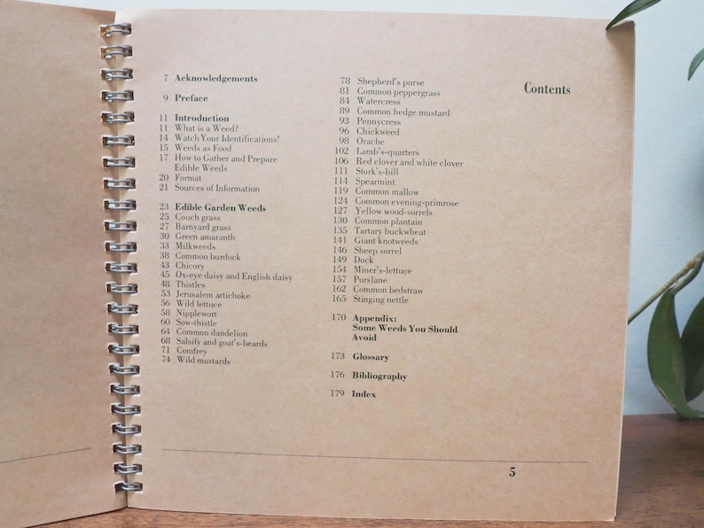May include: Open book with a spiral binding, displaying the contents page. The text lists various edible weeds, including common dandelion and wild mustard. The page has a light brown color.