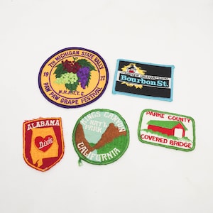 May include: Five embroidered patches with various designs. The top left patch is purple, yellow, and green with the text "7th Michigan State Rally 19 N.H.R.I.T.T.C. 72 Paw Paw Grape Festival". The top right patch is black, blue, and white with the text "New Orleans Bourbon St.". The bottom left patch is red and orange with the text "Alabama Dixie". The bottom middle patch is green and brown with the text "Kings Canyon Nat'l Park California". The bottom right patch is red, white, and green with the text "Parke County Covered Bridge".
