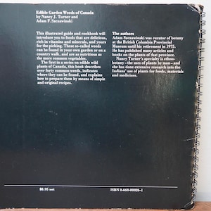 May include: A black book titled "Edible Garden Weeds of Canada" with white text. The book's text describes edible wild plants and recipes. The book has a spiral binding and is slightly worn.