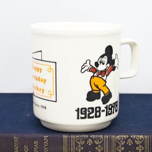 May include: White ceramic mug featuring a cartoon image of Mickey Mouse in a red and yellow outfit. The mug has the text "Happy Birthday Mickey" and "1928-1978" printed on it.