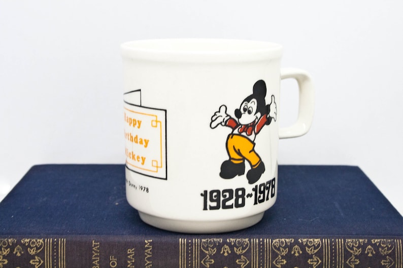 May include: White ceramic mug featuring a cartoon image of Mickey Mouse in a red and yellow outfit. The mug has the text "Happy Birthday Mickey" and "1928-1978" printed on it.