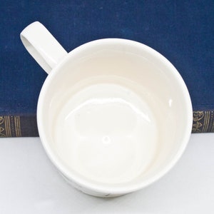 May include: White ceramic mug with a handle. The mug is empty and has a smooth, glossy finish.
