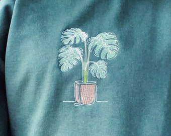 May include: A dark green sweatshirt with an embroidered design of a potted plant with large leaves.