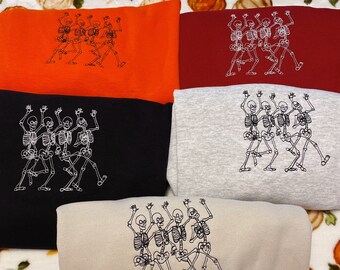 May include: Five different colored sweatshirts with embroidered images of skeletons dancing. The sweatshirts are in orange, red, gray, black, and beige.