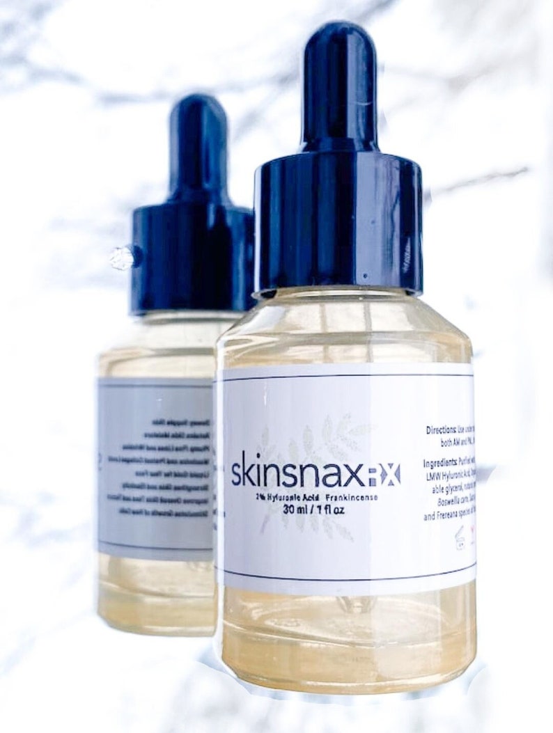 May include: Two clear glass bottles with dropper tops filled with a light yellow liquid. The bottles are labeled "skinsnaxx" and contain 2% Hyaluronic Acid Frankincense, 30 ml / 1 fl oz.