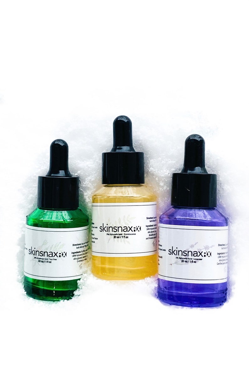 May include: Three glass bottles with dropper tops containing skin care serums. The bottles are labeled "skinsnax:xx" and contain 2% Hyaluronic Acid. The serums are green, yellow, and purple.