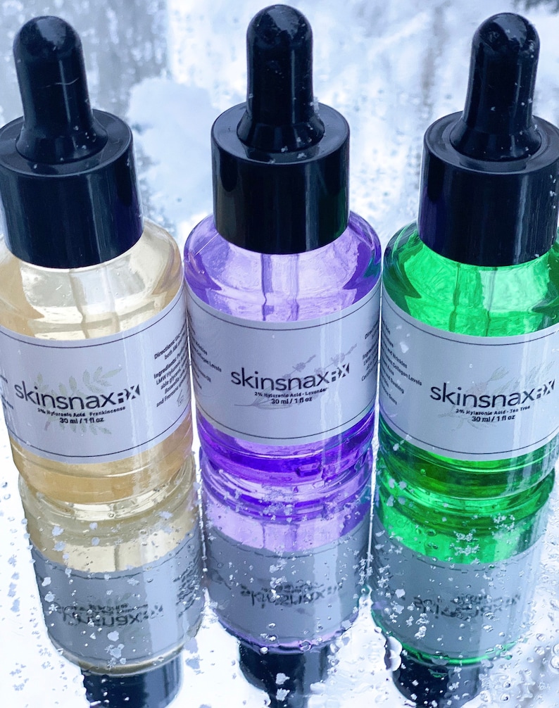 May include: Three glass bottles with dropper tops filled with different colored liquids. The bottles are labeled "skinsnax" and contain 1% Hyaluronic Acid. The bottles are 30 ml / 1 fl oz.