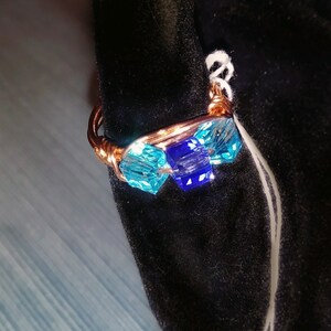 May include: A copper wire ring with blue and turquoise glass beads. The ring is on a black velvet background.