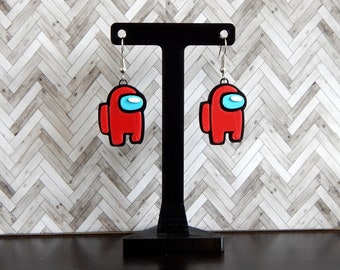 May include: A pair of red Among Us character earrings hanging from a black earring stand. The earrings are made of polymer clay and have a blue visor.