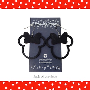 May include: Black Minnie Mouse silhouette earrings with a bow detail. The earrings are displayed on a dark blue card with the text "Rebel Spy Designs" and social media handles. The background is a red border with white polka dots.