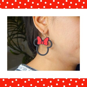 May include: Black Minnie Mouse-shaped earrings with a red bow. These earrings are a playful accessory, ideal for fans of the famous character. The earrings are lightweight and easy to wear, adding a touch of fun to any outfit.