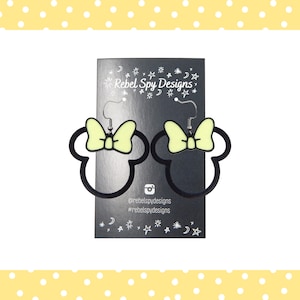 May include: Black outline Minnie Mouse earrings with a light yellow bow. The earrings are displayed on a black card with the text "Rebel Spy Designs" and social media handles. The background is white with a yellow polka dot border.