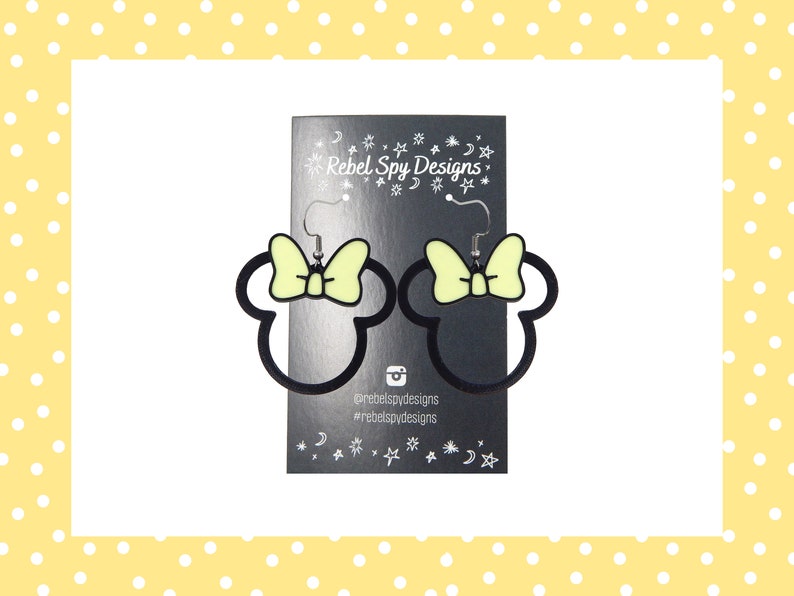 May include: Black outline Minnie Mouse earrings with a light yellow bow. The earrings are displayed on a black card with the text "Rebel Spy Designs" and social media handles. The background is white with a yellow polka dot border.