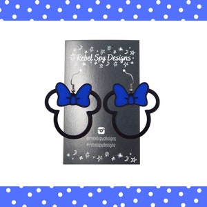 May include: Black outline Minnie Mouse head earrings with a blue bow. The earrings are displayed on a silver card with the text "Rebel Spy Designs" and social media handles. The background is white with a blue polka dot border.
