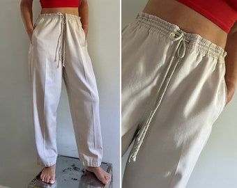 May include: A pair of light beige, wide-leg pants with a drawstring waist. The pants have a relaxed fit and are made of a soft, comfortable fabric.