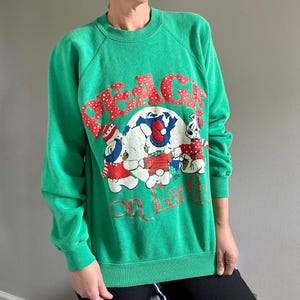 May include: Green Christmas sweatshirt with a white, red, and blue graphic of polar bears holding hands around a globe. The graphic says "Peace on Earth" with white polka dots around the word "Peace".