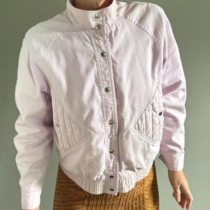 May include: A light purple corduroy jacket with a high collar and snap button fastening. The jacket features a quilted design on the front and back.