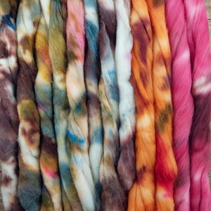 May include: A collection of colorful hand-dyed yarn skeins in shades of brown, orange, pink, blue, and white. The yarn is arranged in rows and is ready for knitting or crocheting.