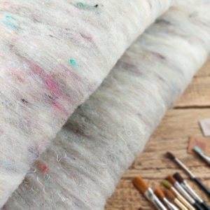 May include: Two layers of white felted fabric with flecks of pink, blue, and green. The fabric is folded in half and the edges are visible.