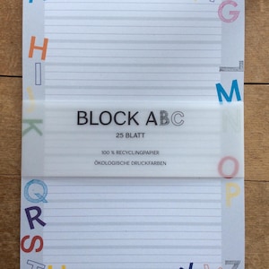 Könnte beinhalten: Ein weißer Notizblock mit einem bunten Alphabet-Rand. Der Notizblock hat liniertes Papier und eine Kopfzeile mit dem Text "BLOCK ABC 25 BLATT 100% RECYCLINGPAPIER ÖKOLOGISCHE DRUCKFARBEN".