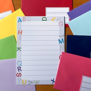 Könnte beinhalten: Ein weißes, liniertes Blatt Papier mit einem grauen Rand und bunten Buchstaben, die das Alphabet um den Rand herum buchstabieren. Das Papier ist von bunten Umschlägen umgeben.
