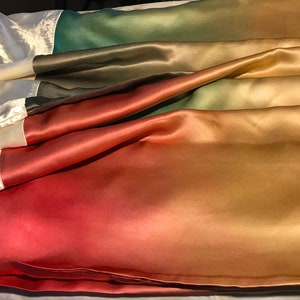 May include: A gradient fabric with a white, green, red, orange, and gold color scheme. The fabric is made of satin and has a smooth, silky texture.