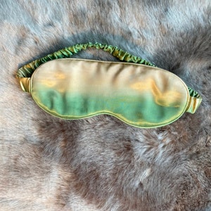 May include: A green and gold silk sleep mask with a gathered elastic band.