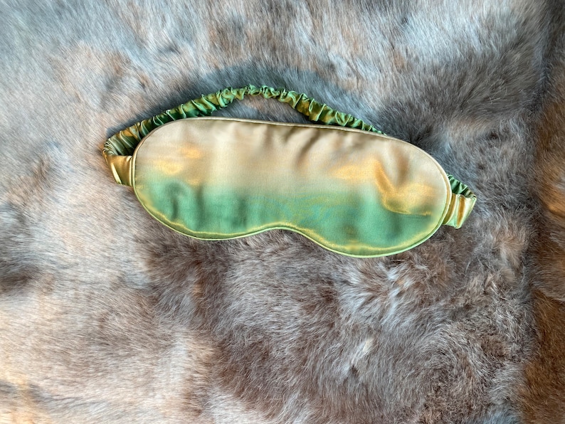 May include: A green and gold silk sleep mask with a gathered elastic band.