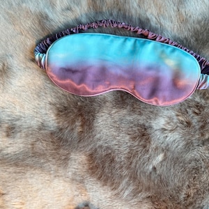 May include: A purple and blue ombre sleep mask made of satin.