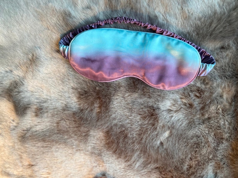 May include: A purple and blue ombre sleep mask made of satin.