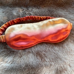 May include: A soft, silky sleep mask with a gradient color design, transitioning from a light gold to a deep orange.