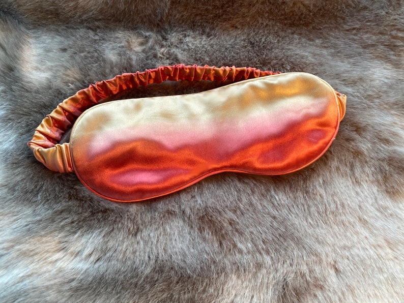 May include: A soft, silky sleep mask with a gradient color design, transitioning from a light gold to a deep orange.