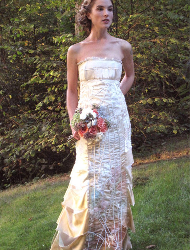 May include: A white strapless wedding dress with a layered skirt and a delicate floral pattern. The dress is made of a soft, flowing fabric and has a romantic, ethereal feel.