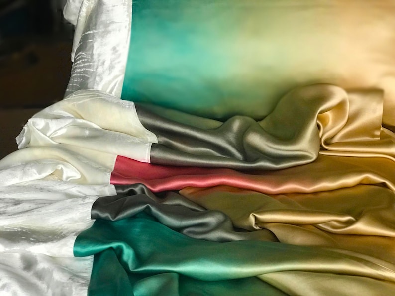 May include: A set of five silk pillowcases in various shades of green, gold, and red. The pillowcases are arranged in a layered, cascading pattern, showcasing the smooth, luxurious texture of the fabric.