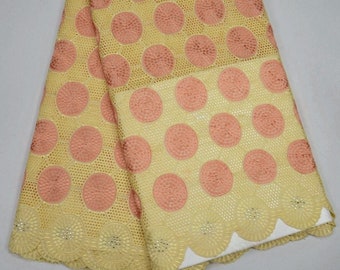 May include: A yellow and peach lace fabric with a circular pattern. The fabric has a scalloped edge and is decorated with small rhinestones.