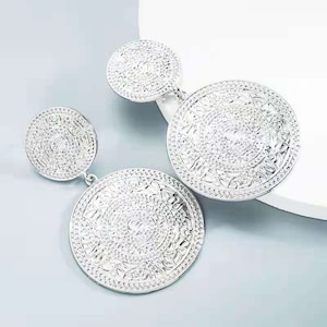 May include: A pair of silver dangle earrings with two circular discs. The larger disc has a detailed, intricate pattern.