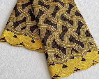 May include: A piece of dark brown lace fabric featuring a repeating pattern of golden yellow embroidered wavy lines. The fabric has a scalloped edge along the bottom, with a mesh-like texture throughout the dark brown sections of the material.