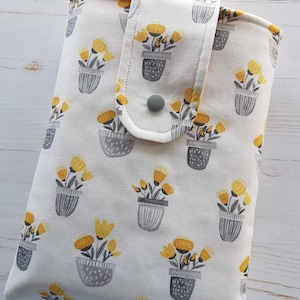 May include: A white fabric pouch with a flap closure and a snap button. The pouch has a floral pattern with yellow flowers in grey pots.