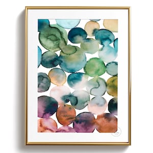 Puede incluir: Lámina de arte abstracto en acuarela en un marco dorado. La obra presenta círculos superpuestos en tonos de verde azulado, verde, morado y naranja sobre un fondo blanco. La impresión es una pieza moderna de decoración mural.