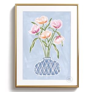 Peut inclure: Une impression d'art encadrée représentant une nature morte florale. L'œuvre représente des fleurs roses et pêche dans un vase bleu à motifs de losanges, sur fond bleu clair. Le cadre est doré.