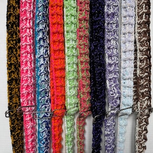 May include: A collection of colorful, crocheted straps in various hues, including black, pink, blue, orange, green, purple, and brown. Each strap is secured with a silver metal clip. The textured crochet design adds visual interest to these handmade accessories.
