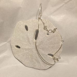 Peut inclure: Ornement en forme de dollar de sable blanc avec un fil d'argent et des perles transparentes. L'ornement est conçu pour être suspendu à un arbre de Noël.