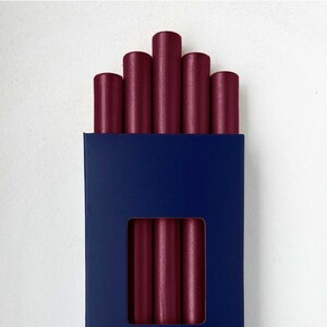 Puede incluir: Una caja de seis barras de cera de sellado color burdeos. La caja es azul con letras doradas que dicen "SIEGELWACHS...direkt aus der Siegelwerkstatt".